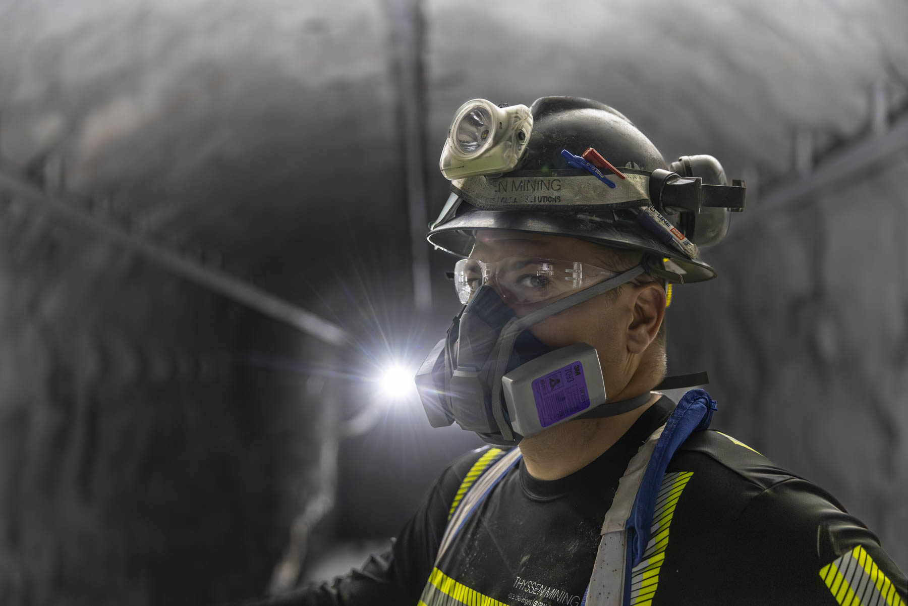 Underground miner portrait wearing a helmet, headlamp, eye protection, and respirator