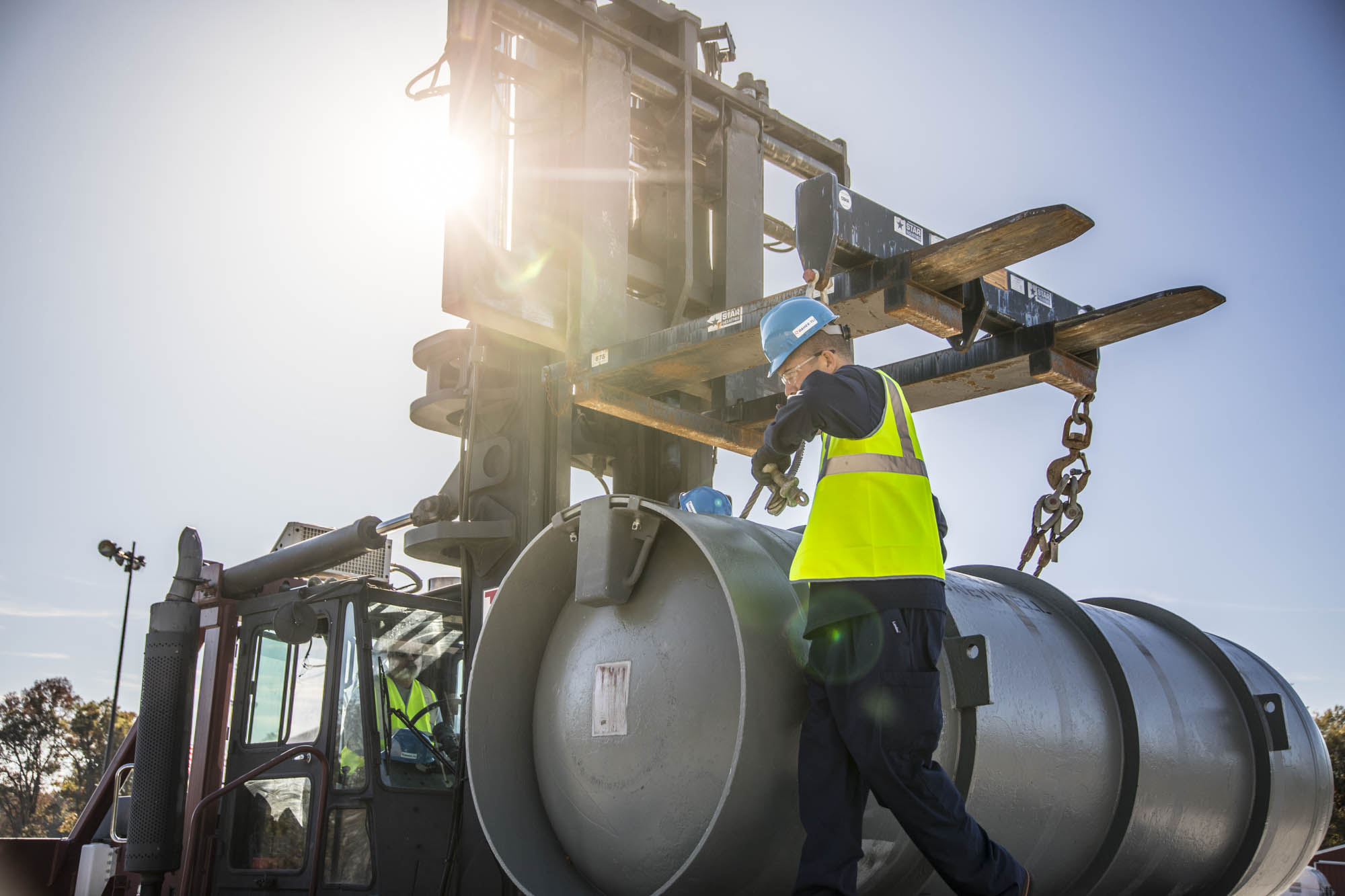 Forklift operator guiding stacked casks into position outdoors