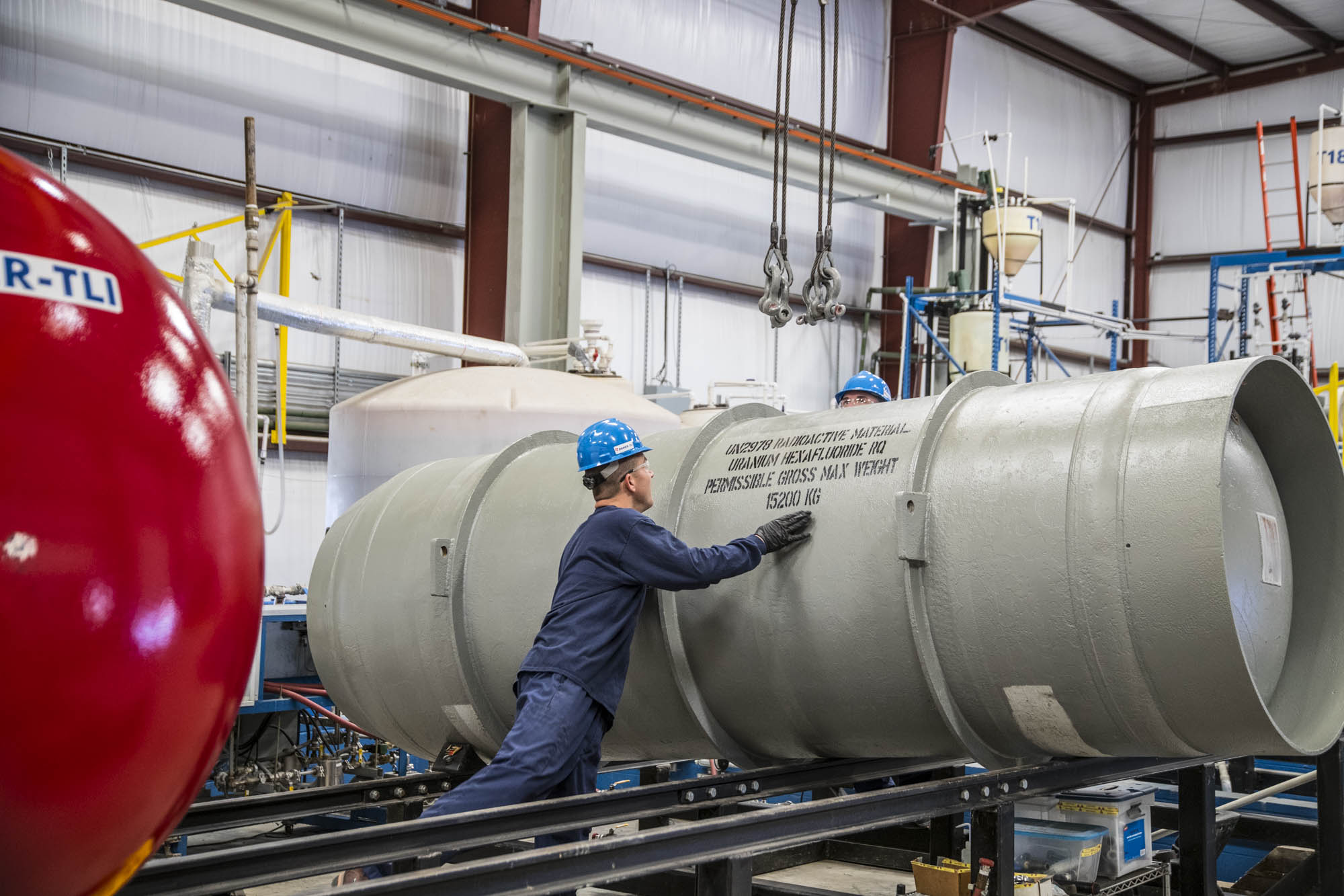 Technician inspecting a uranium hexafluoride transport cask stenciled with weight and hazard markings