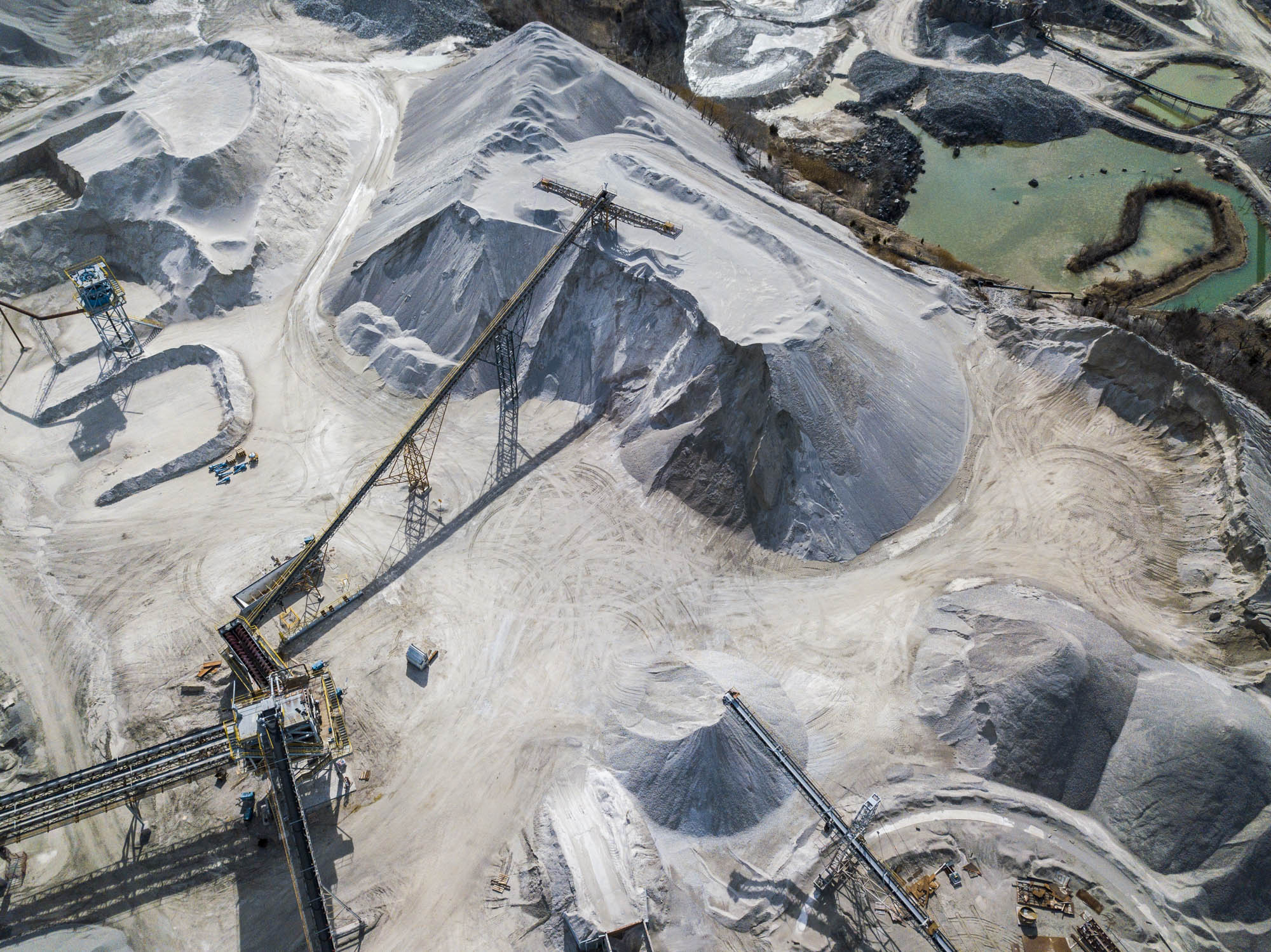 Aerial view of a stockpile and conveyor beside a quarry settling pond