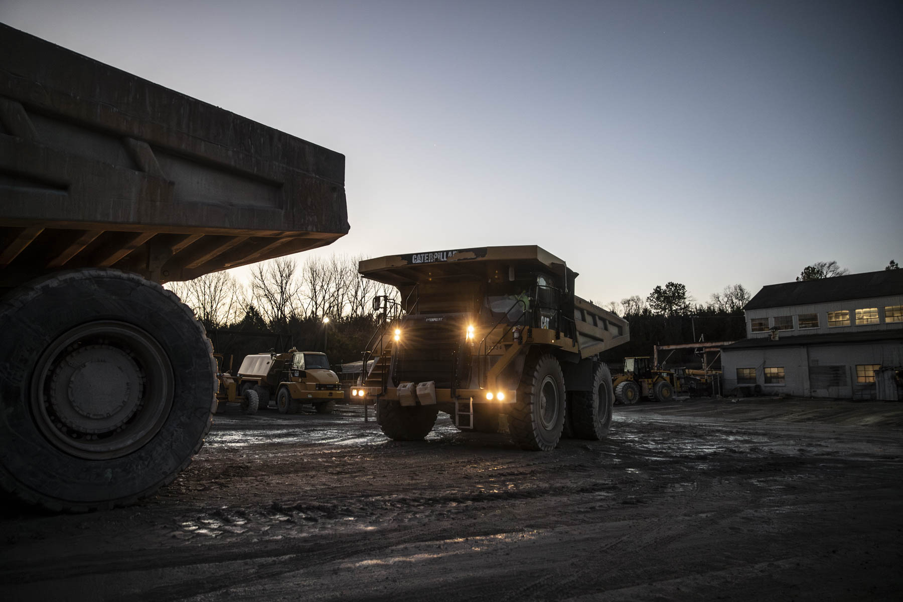 Mining haul truck operating at dusk between heavy-equipment silhouettes