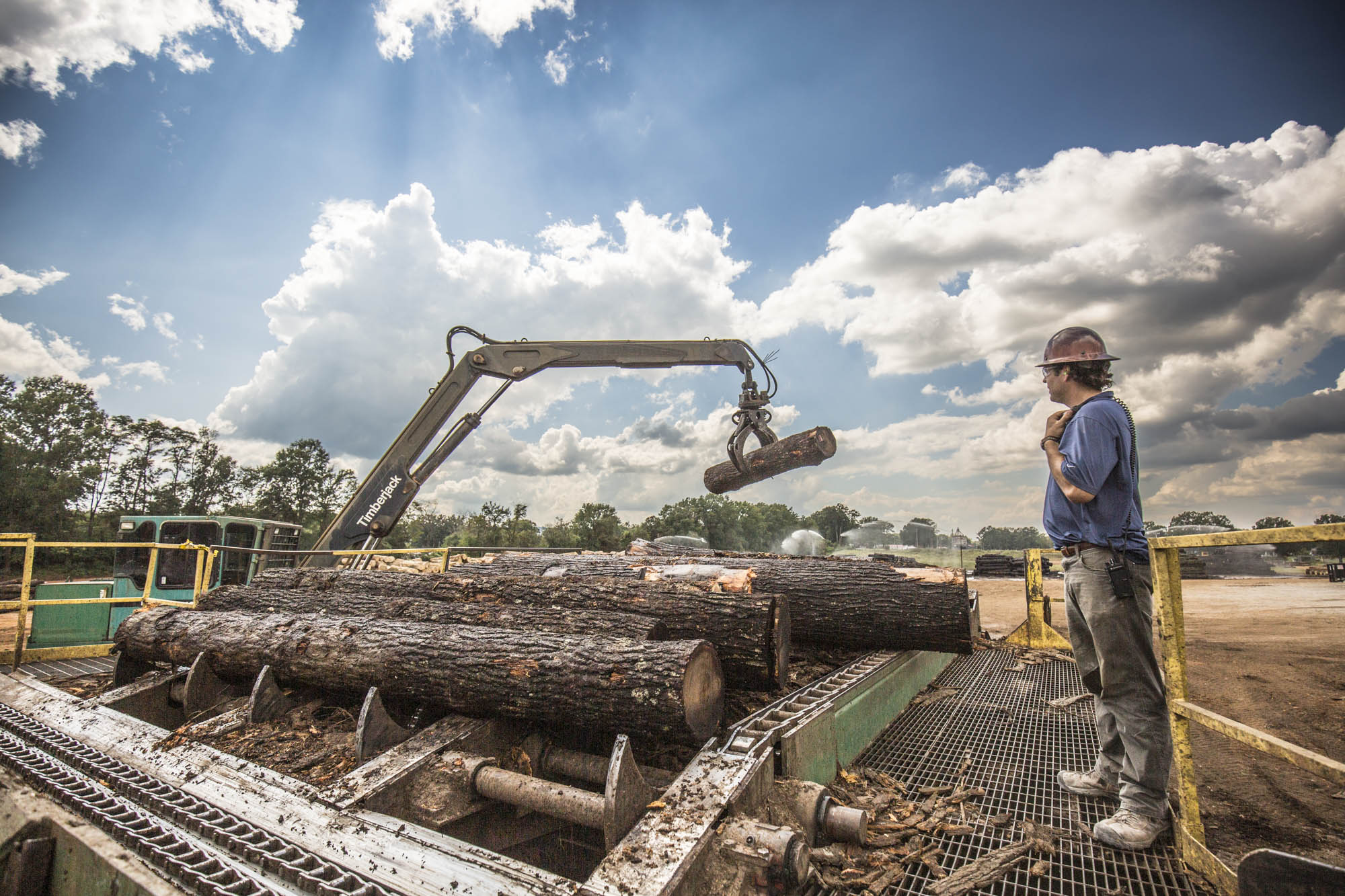 Hydraulic loader grappling logs onto the mill infeed deck