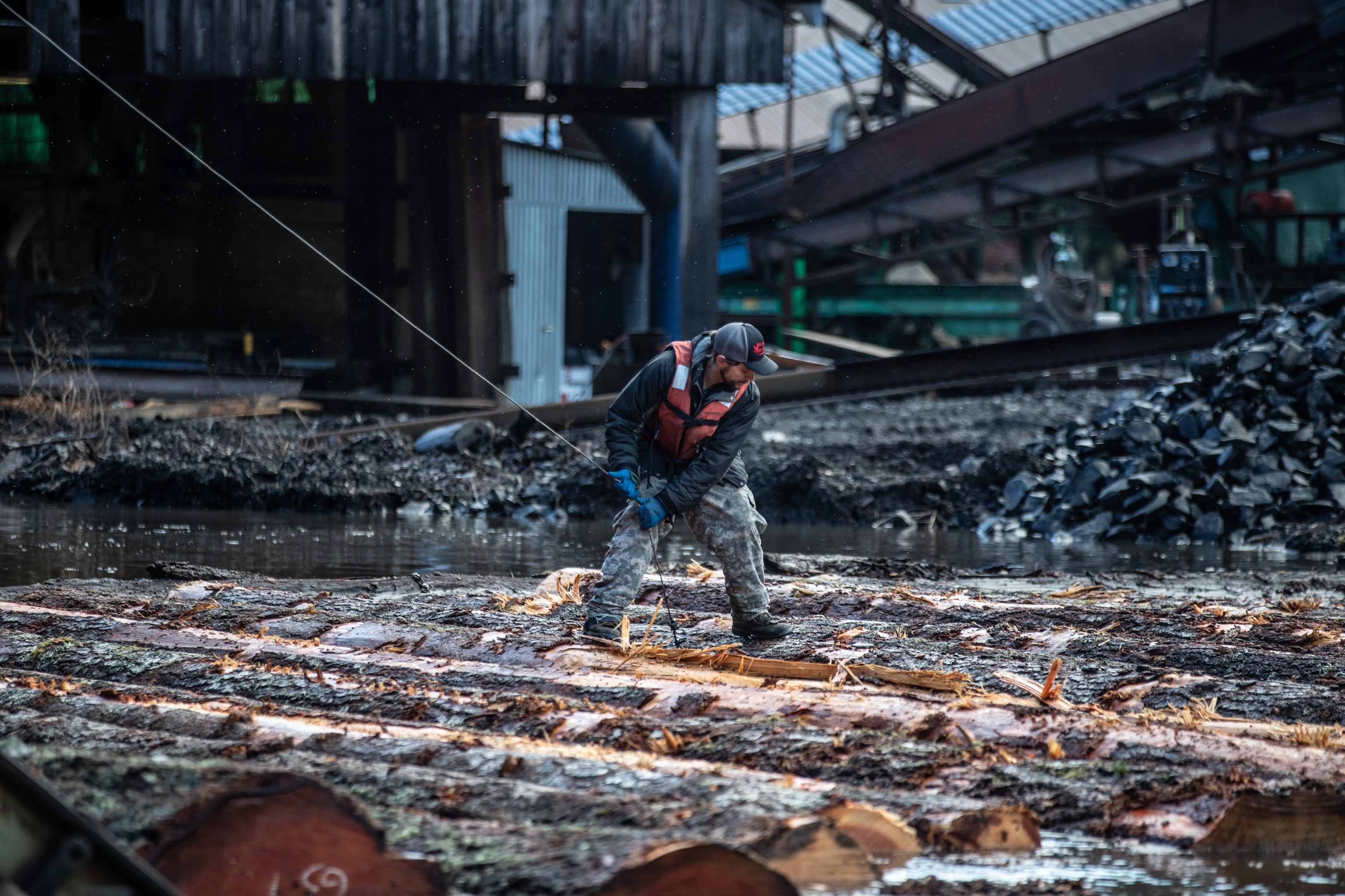 Log pond worker maneuvering floating timber at an active sawmill